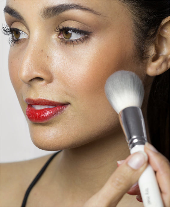 a vegan eco friendly powder brush for makeup bronzer and blush. Woman applying blush powder with brush. 